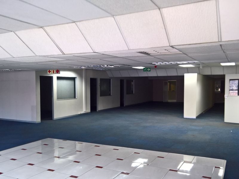 Spacious open-plan industrial office area featuring a mix of carpet and tiled flooring, suspended ceilings, and integrated fire safety equipment.