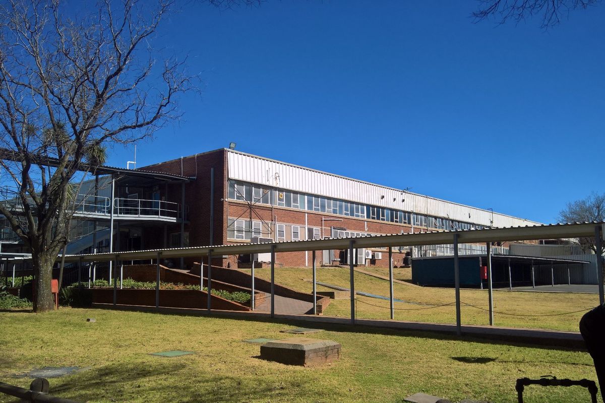 Rear view of a large industrial building featuring brick construction, extensive multi-pane windows, and a covered pedestrian walkway connecting the facility.