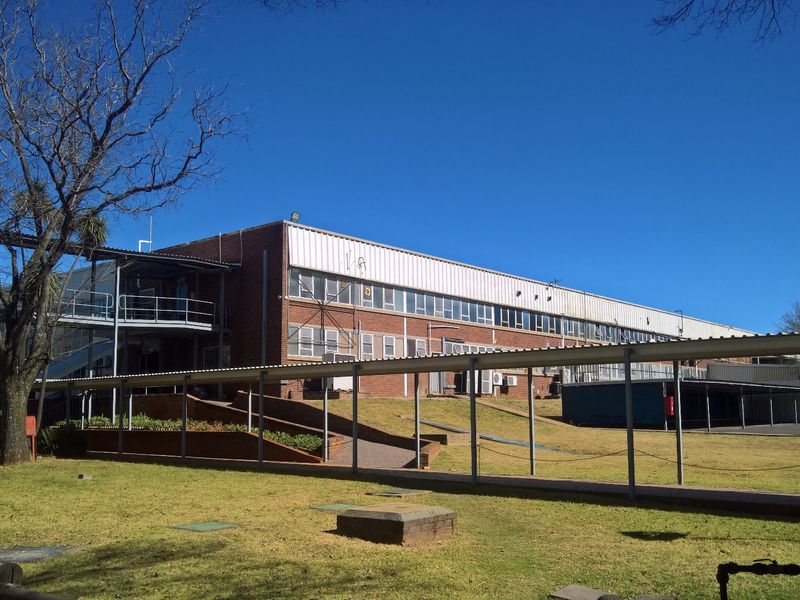 Rear view of a large industrial building featuring brick construction, extensive multi-pane windows, and a covered pedestrian walkway connecting the facility.