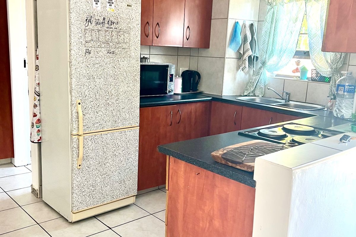 A functional kitchen featuring wood-finish cabinetry, dark laminate countertops, a double basin sink, and ceramic tile flooring throughout.
