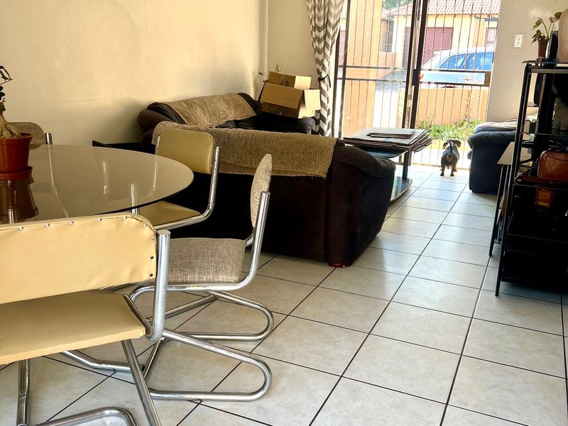 Open-plan living and dining area featuring ceramic floor tiles, recessed lighting, and a sliding glass door with security gate leading to the exterior.