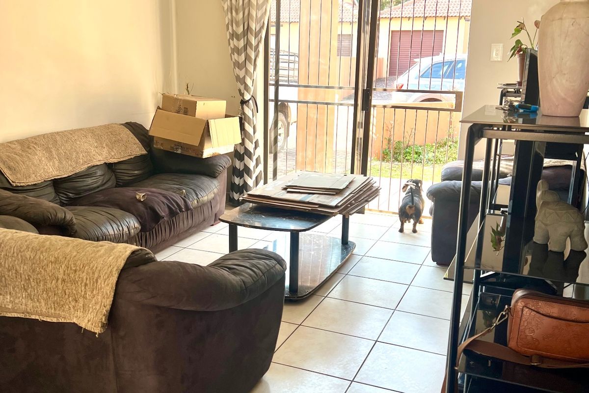 A living room featuring tiled flooring and a sliding glass door with a security gate, providing access to the exterior.