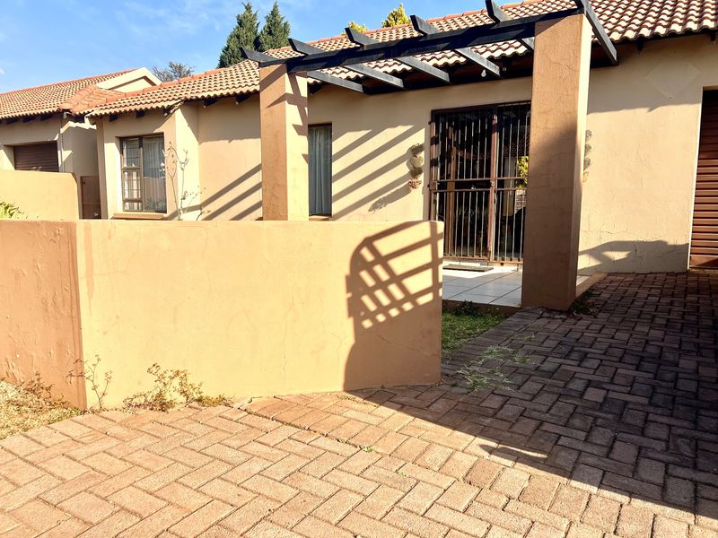 Front exterior view of a townhouse featuring a paved driveway, a covered pergola entrance, and a secure gated entry.