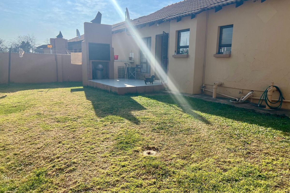 Rear view of the townhouse featuring a private garden, a tiled patio area with a built-in braai, and perimeter walling.