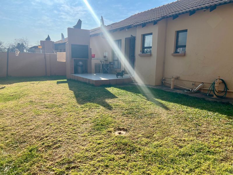 Rear view of the townhouse featuring a private garden, a tiled patio area with a built-in braai, and perimeter walling.