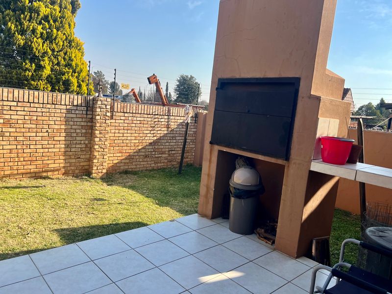 Outdoor patio area featuring a built-in braai, tiled flooring, and a private garden space enclosed by a brick boundary wall with electric fencing.