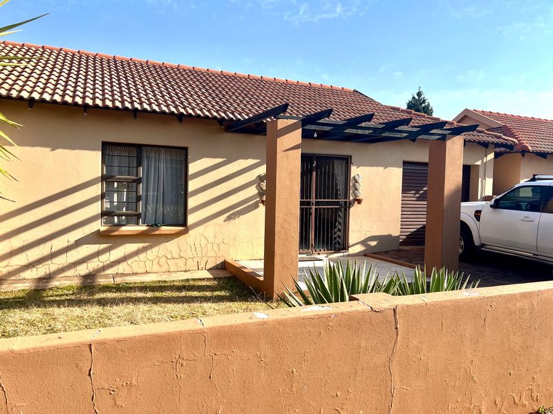 Front elevation of a townhouse featuring a tiled roof, a pergola over the entrance, and a paved driveway with a boundary wall.