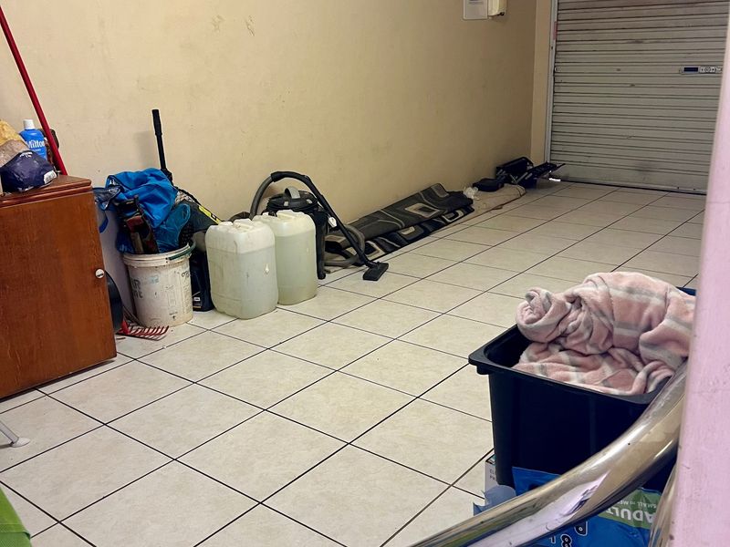 A functional garage space featuring tiled flooring and a secure roller shutter door, currently used for storage.