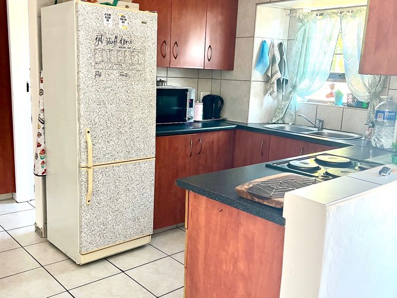 A functional kitchen featuring wood-finish cabinetry, dark laminate countertops, a double basin sink, and ceramic tile flooring throughout.