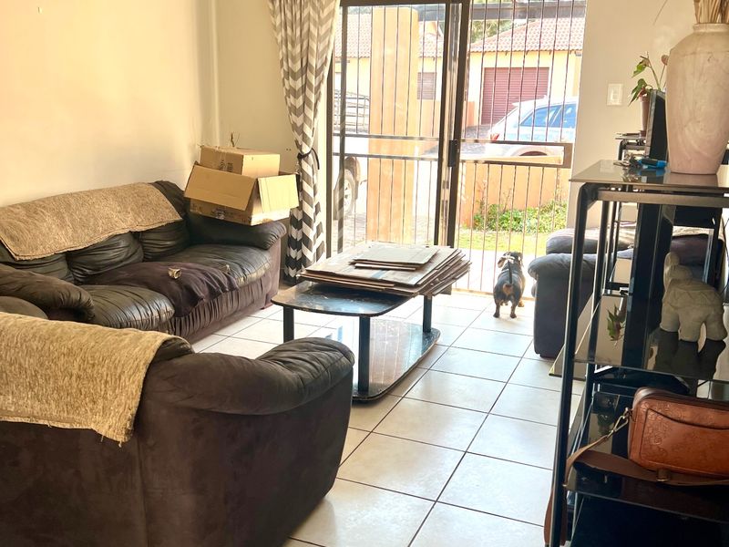 A living room featuring tiled flooring and a sliding glass door with a security gate, providing access to the exterior.