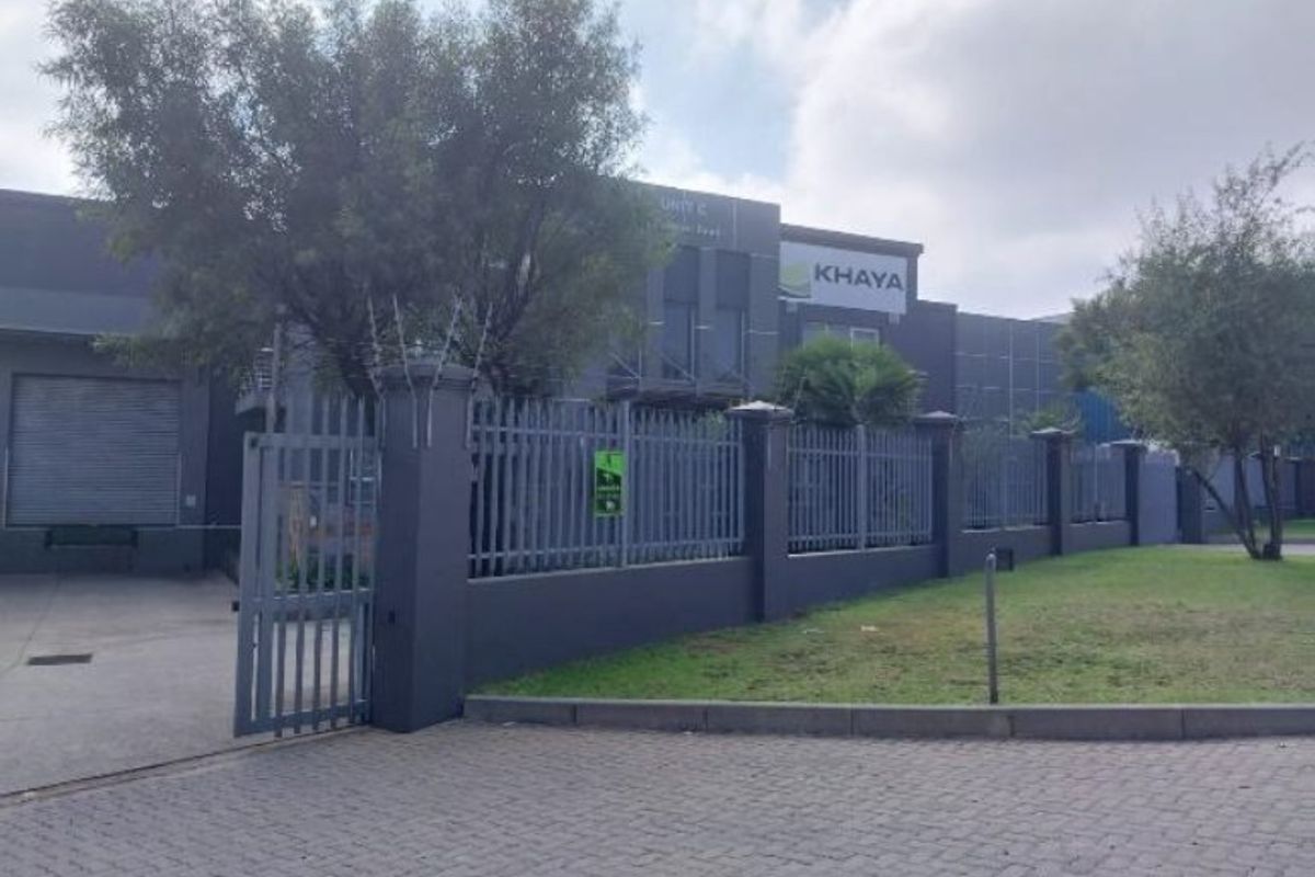 Front exterior view of an industrial property featuring a secure steel palisade fence, gated entrance, paved driveway, and a large roller shutter door.