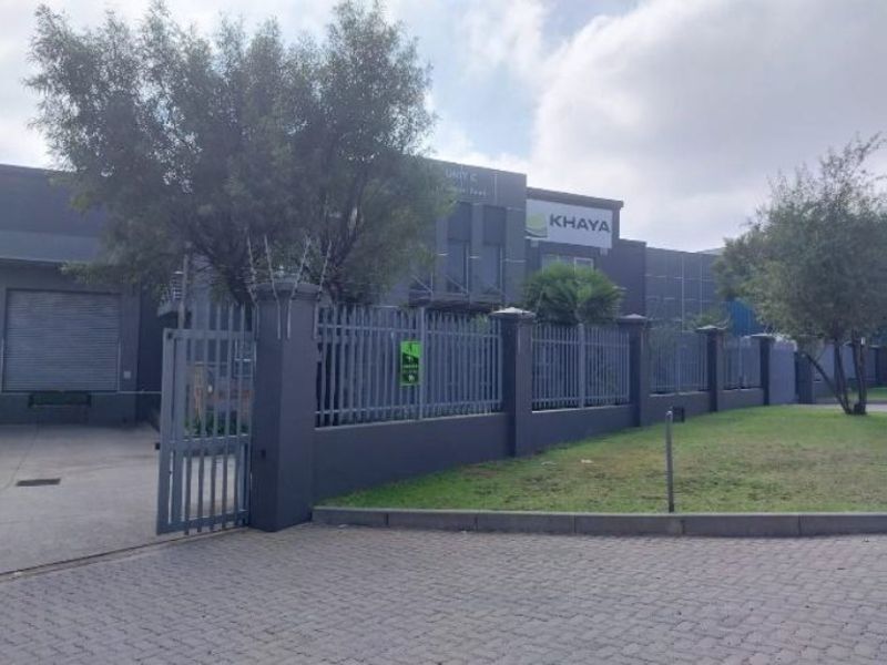 Front exterior view of an industrial property featuring a secure steel palisade fence, gated entrance, paved driveway, and a large roller shutter door.