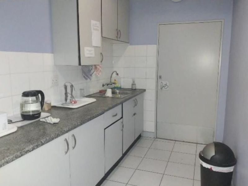 A functional kitchenette featuring laminate countertops, stainless steel sink, tiled backsplash, and built-in cabinetry, suitable for office or industrial utility use.