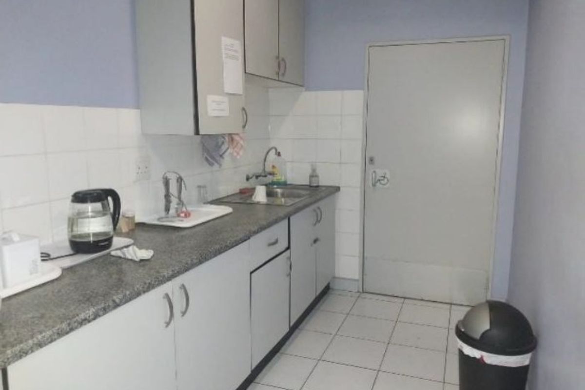 A functional kitchenette featuring laminate countertops, stainless steel sink, tiled backsplash, and built-in cabinetry, suitable for office or industrial utility use.