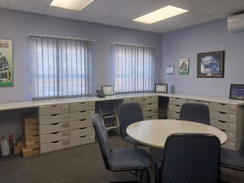 A functional office space featuring extensive built-in cabinetry, vertical blinds, recessed lighting, and a wall-mounted air conditioning unit.