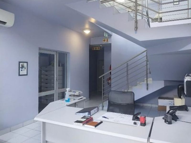 Industrial office entry area featuring a staircase with stainless steel balustrades, tiled flooring, and a reception desk setup.