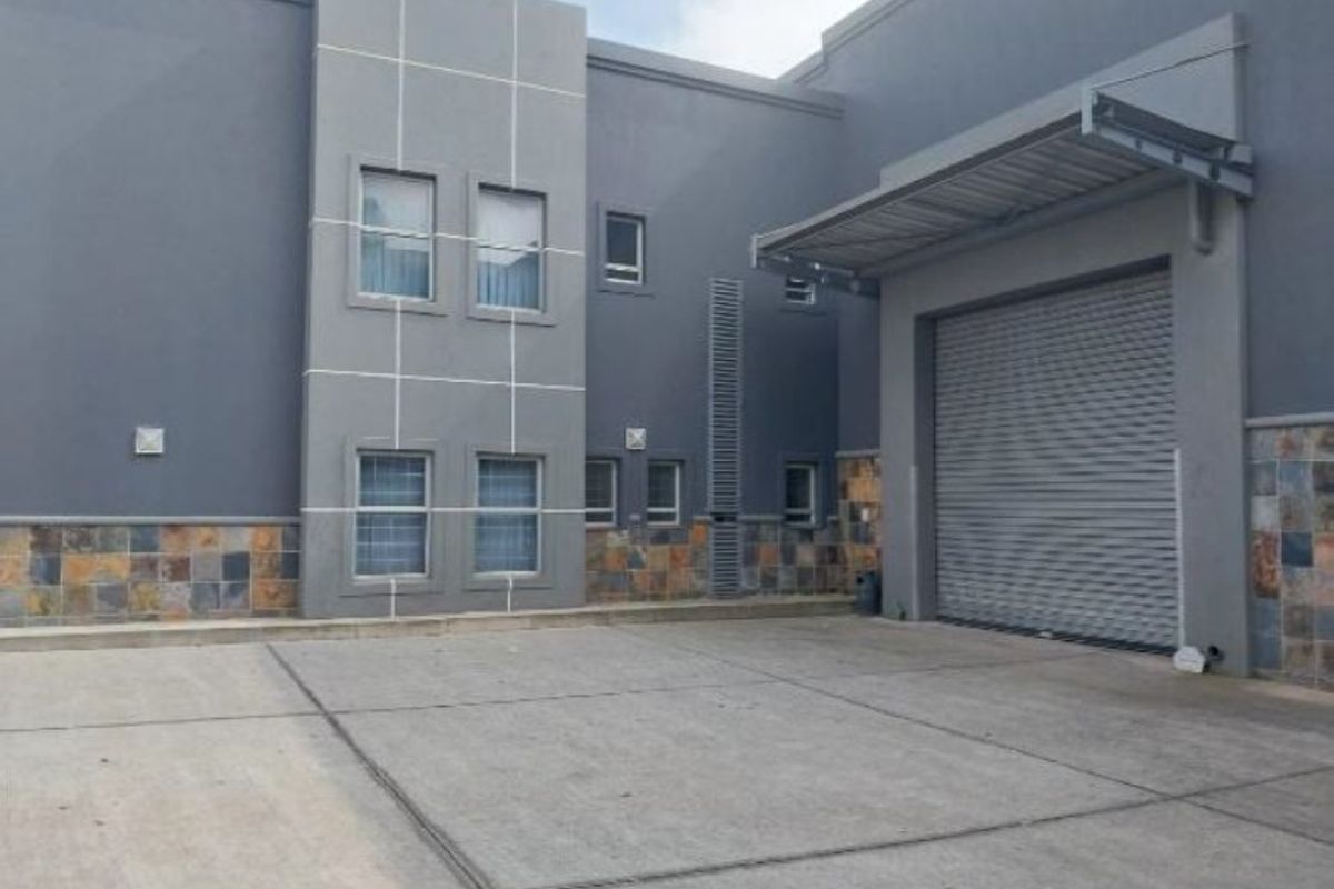 Industrial property exterior featuring a concrete driveway, roller shutter door, and modern stone-clad facade with metal awning.