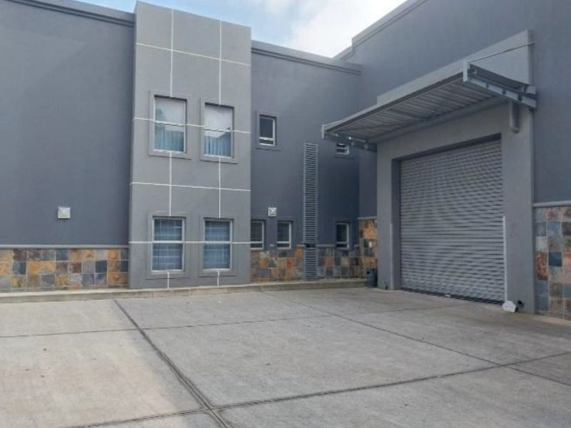 Industrial property exterior featuring a concrete driveway, roller shutter door, and modern stone-clad facade with metal awning.