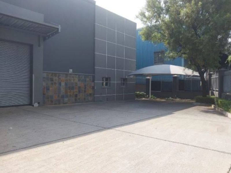 Industrial property exterior featuring a concrete driveway, roller shutter door, and a shade sail carport for vehicle parking.