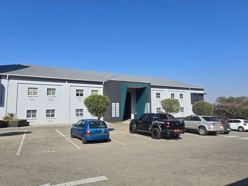 Front exterior view of a commercial office building featuring a paved parking lot, landscaped trees, and prominent signage.