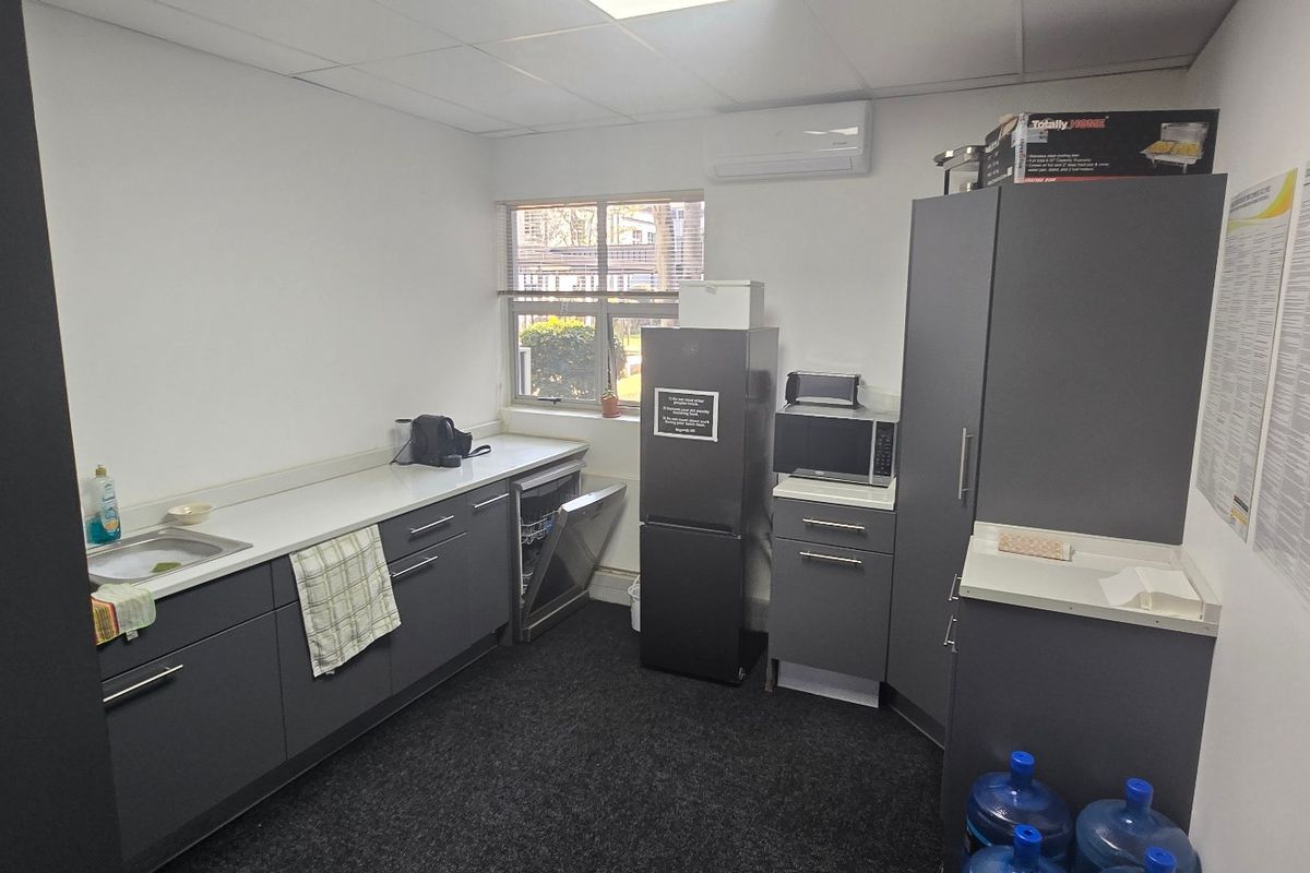 A functional commercial kitchenette featuring dark grey cabinetry, a sink, integrated dishwasher, and a wall-mounted air conditioning unit.