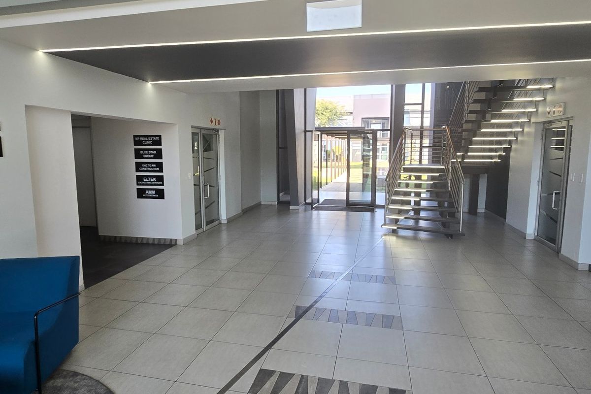 Modern commercial building entrance lobby featuring tiled flooring, a central staircase with integrated lighting, and professional tenant directory signage.