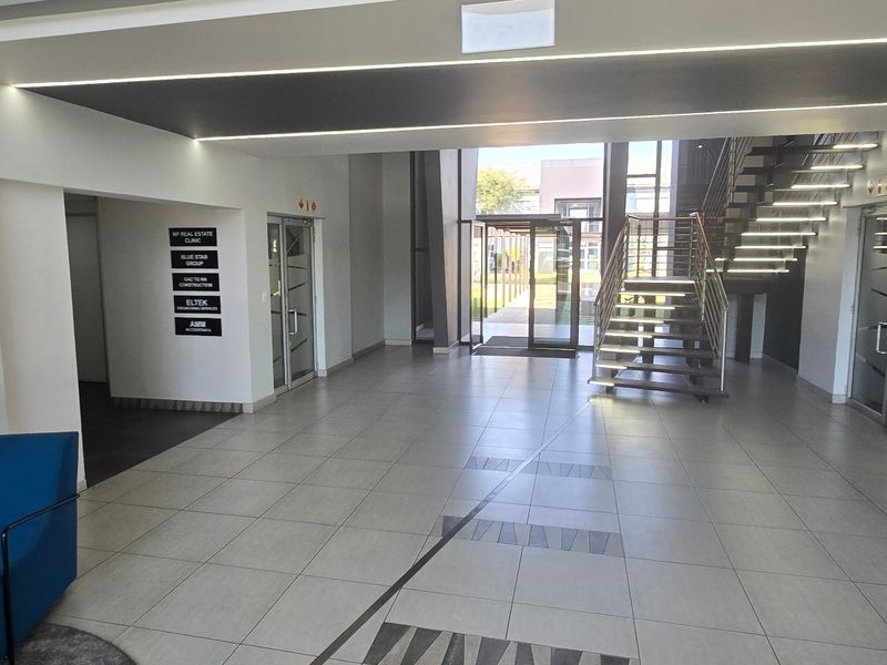 Modern commercial building entrance lobby featuring tiled flooring, a central staircase with integrated lighting, and professional tenant directory signage.