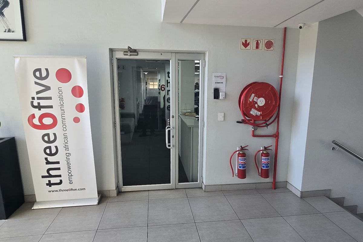 Commercial office entrance featuring a glass door, tiled flooring, and essential fire safety equipment including a hose reel and extinguishers.