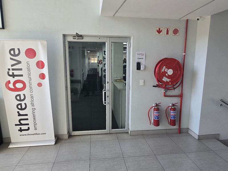 Commercial office entrance featuring a glass door, tiled flooring, and essential fire safety equipment including a hose reel and extinguishers.
