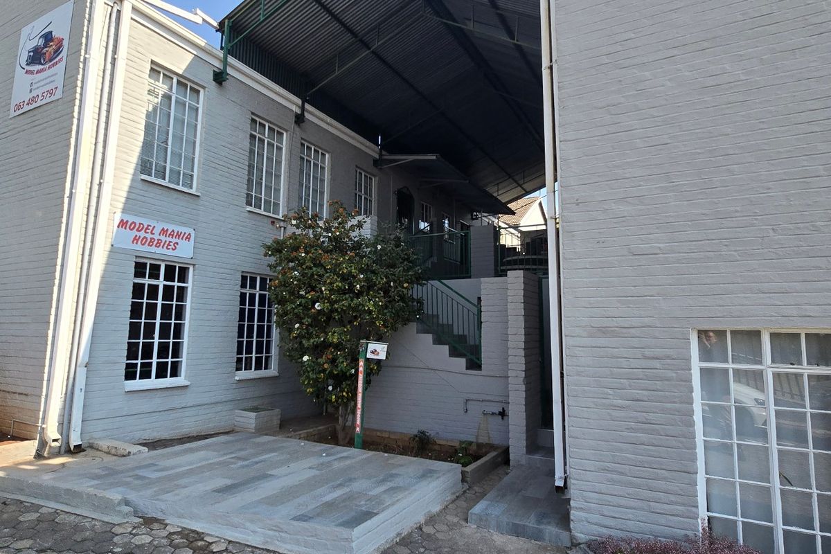 Rear exterior view of a commercial building featuring painted brick walls, lattice windows, a paved courtyard area, and an external staircase under a metal roof.