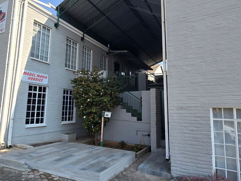 Rear exterior view of a commercial building featuring painted brick walls, lattice windows, a paved courtyard area, and an external staircase under a metal roof.