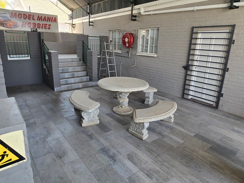 A covered outdoor patio area featuring tiled flooring, brick walls, a security gate, and a staircase leading to an elevated section.
