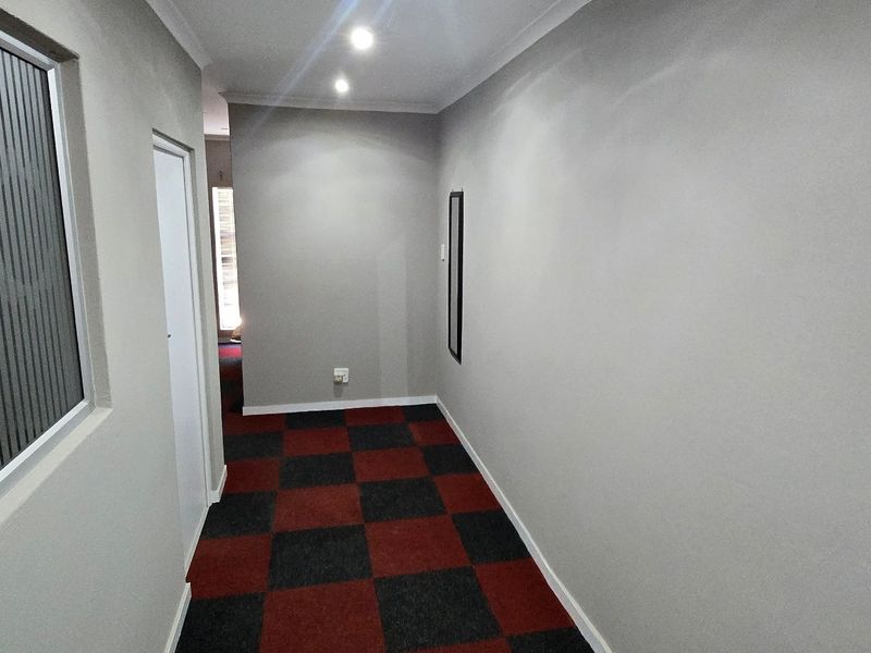 A clean, well-lit commercial hallway featuring modern grey walls, red and black checkered carpet tiles, and a frosted glass office partition.