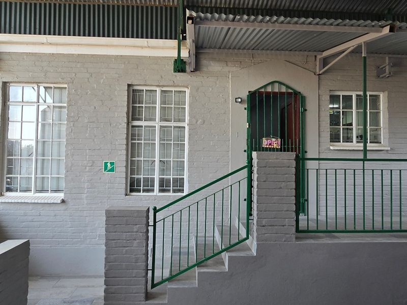 Commercial building exterior featuring a painted brick facade, steel-framed windows, and a covered entrance with metal security gate and stairs.