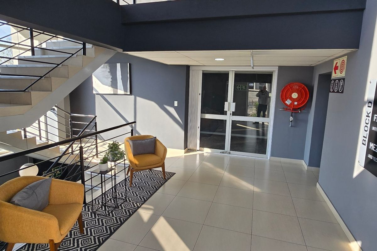 Modern commercial building entrance lobby featuring tiled flooring, a prominent staircase with metal balustrades, and clear directional signage for office levels.