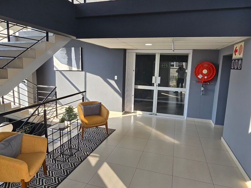 Modern commercial building entrance lobby featuring tiled flooring, a prominent staircase with metal balustrades, and clear directional signage for office levels.