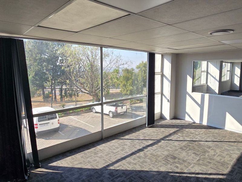 A bright, vacant office space featuring large windows with exterior views, carpeted flooring, and a suspended ceiling, suitable for a professional workspace.