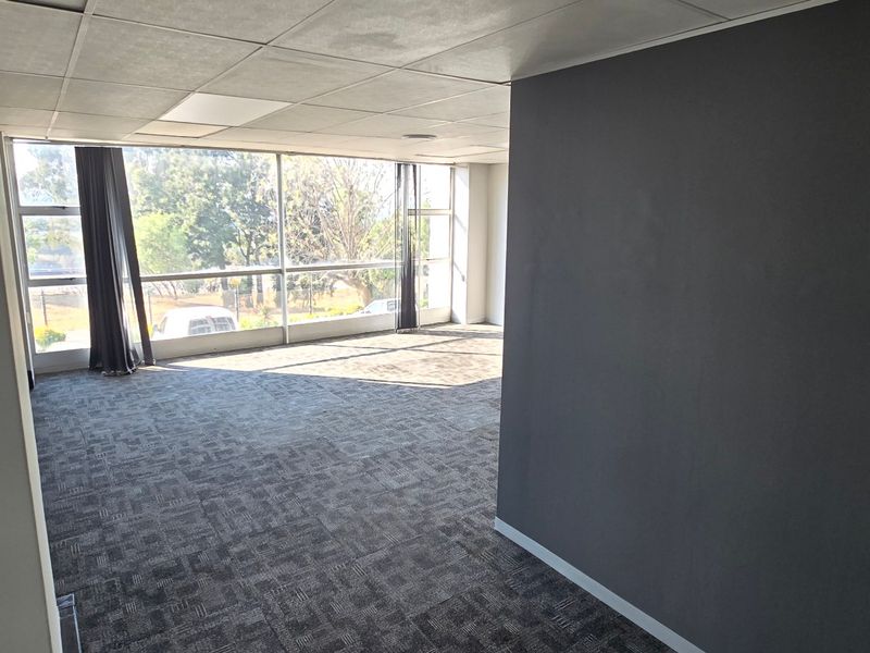 A bright, empty office space featuring large windows, carpeted flooring, and a suspended ceiling, offering a clean and professional environment.