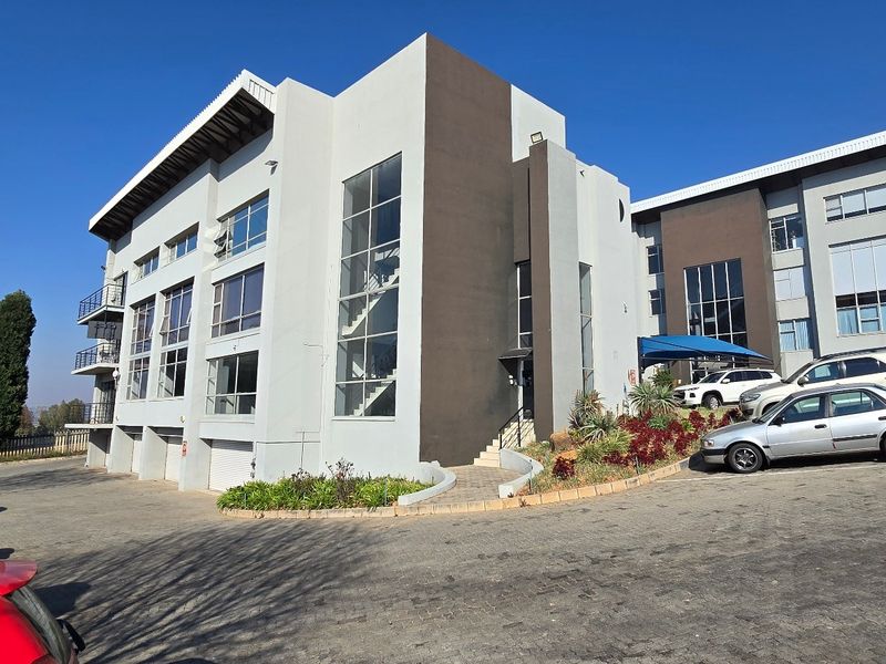 A modern multi-story commercial building featuring a contemporary facade with extensive glass paneling, paved parking, and well-maintained landscaped garden areas.