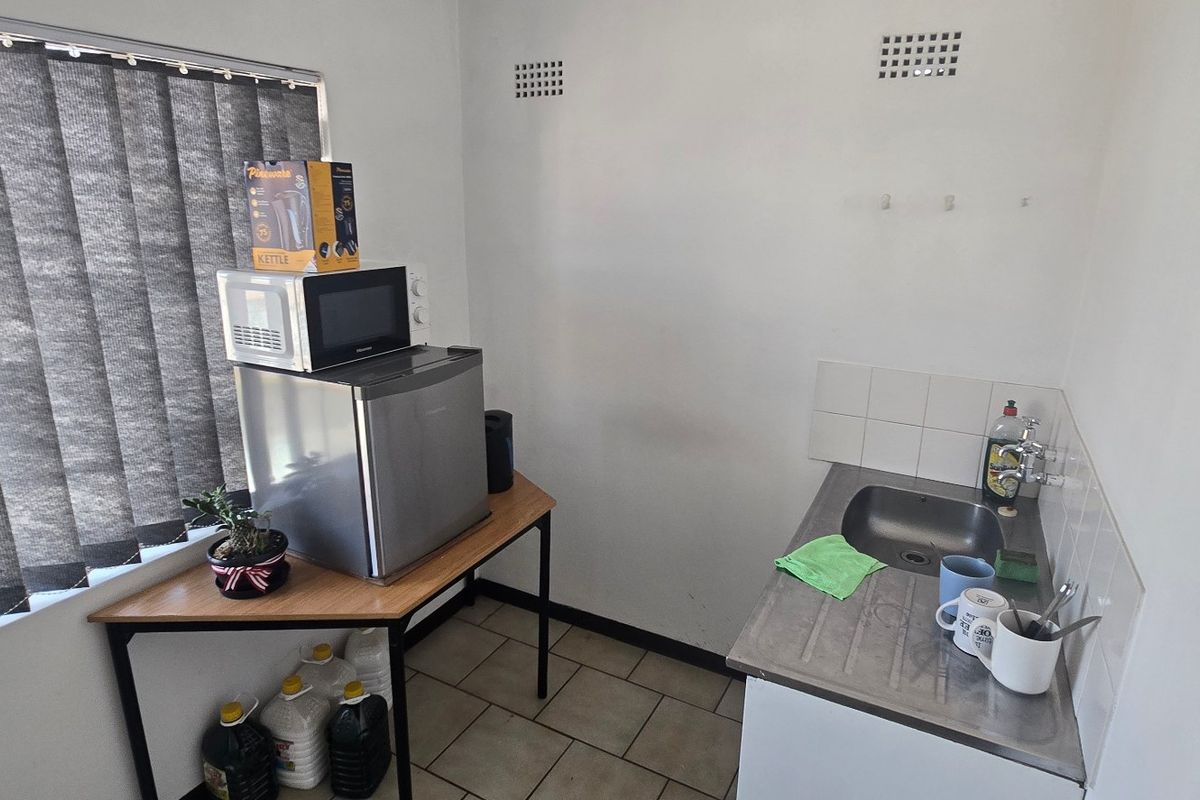A compact kitchenette featuring a stainless steel sink, tiled splashback, and ceramic floor tiles, suitable for a small office or utility space.