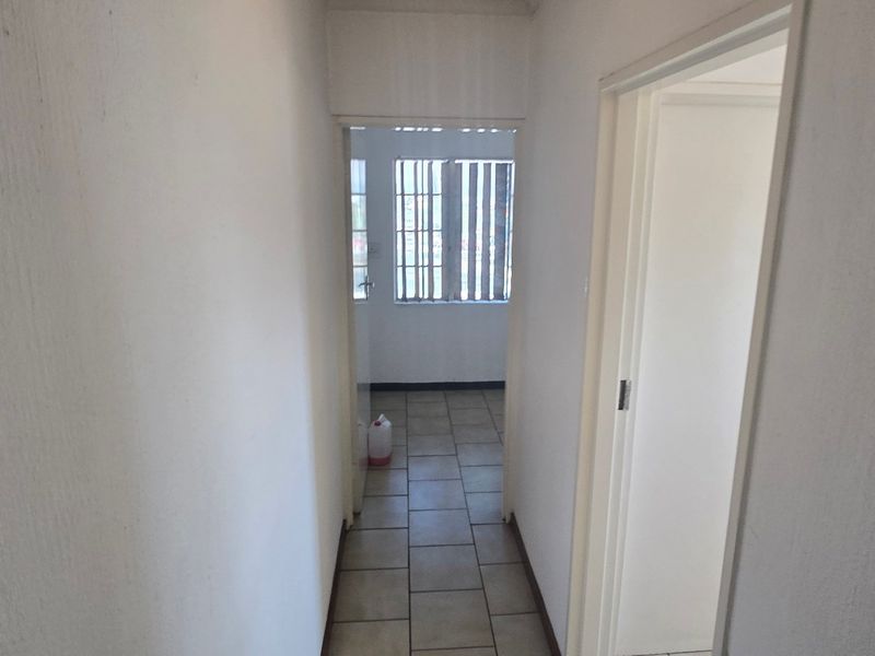 A simple, empty hallway with tiled flooring leading to an adjacent room with window security bars.