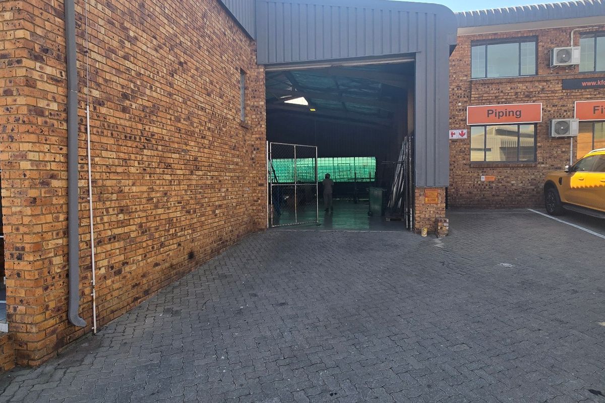Industrial property exterior featuring a face brick facade, paved driveway, secure entrance gate, and roller shutter access to the warehouse space.