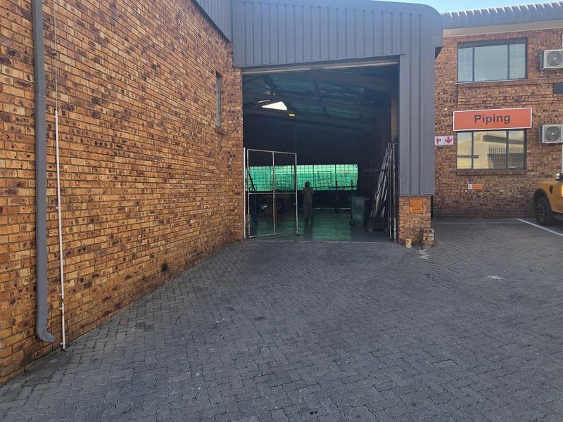 Industrial property exterior featuring a face brick facade, paved driveway, secure entrance gate, and roller shutter access to the warehouse space.