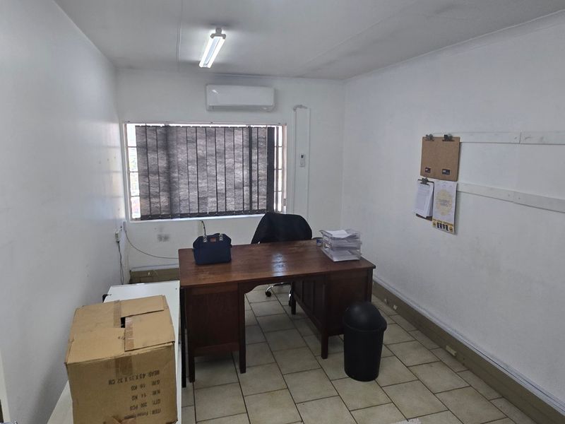 A functional office space featuring tiled flooring, a wall-mounted air conditioning unit, and overhead fluorescent lighting.