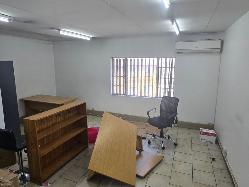 A functional office space featuring tiled flooring, a wall-mounted air conditioning unit, and fluorescent lighting, suitable for a professional workspace.