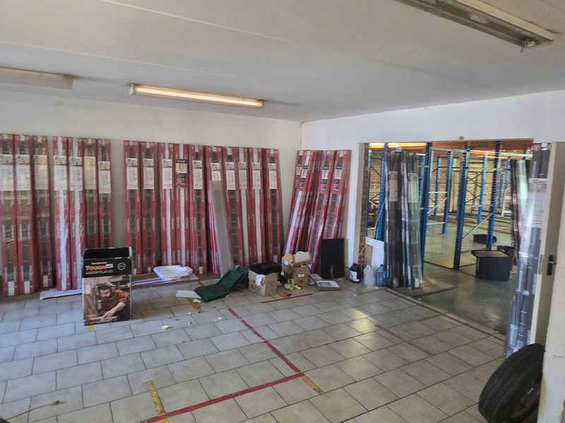Industrial utility space featuring tiled flooring, fluorescent lighting, and an open transition to a storage area with industrial racking.