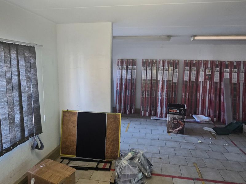 A functional utility or storage space featuring tiled flooring, fluorescent lighting, and vertical window blinds, currently used for storage.