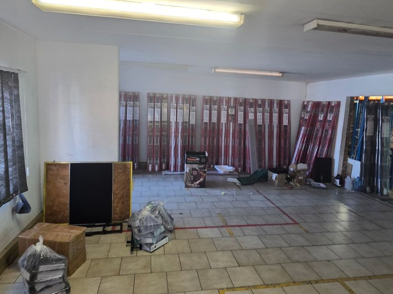 Open-plan industrial office space featuring tiled flooring, fluorescent lighting, and vertical blinds, offering a versatile layout for various business operations.