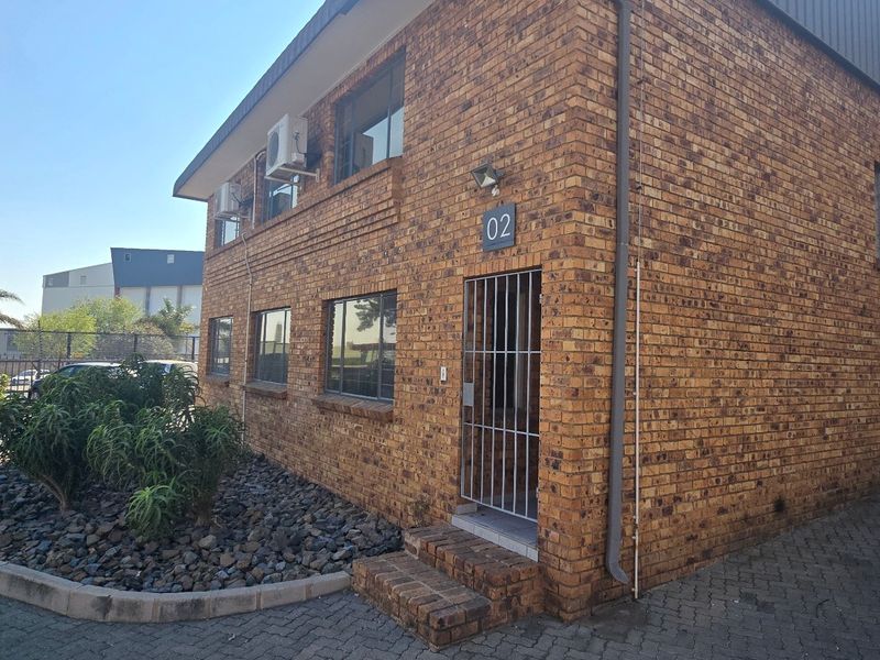 Front elevation of an industrial unit featuring face brick construction, security gate entrance, and an integrated roller shutter door for warehouse access.
