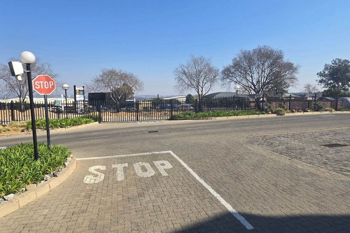 A paved industrial property entrance featuring secure metal fencing, gated access, and clear traffic signage.